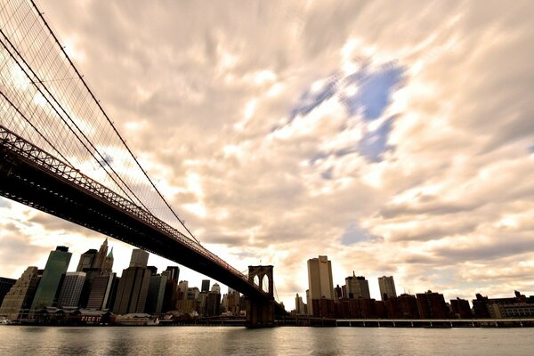 Blick von unten vom Fluss auf die Brooklyn Bridge, Manhattan und die Wolken