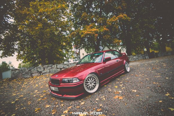 Voiture BMW rouge sur la route parsemée de feuilles jaunes