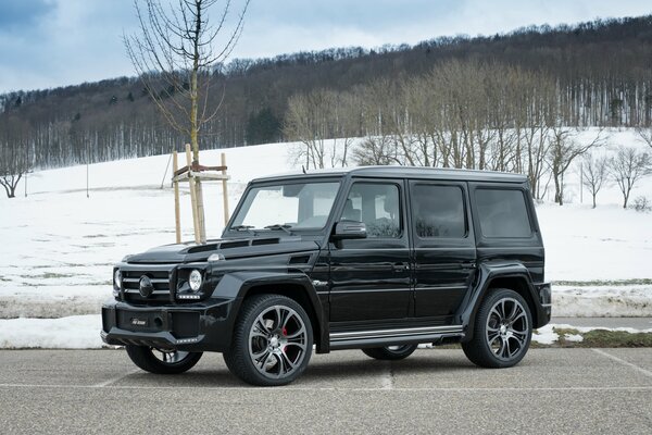 Mercedes negro en la calle. En el fondo hay nieve y árboles desnudos. Parece una primavera