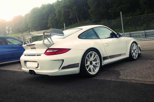 Photo of a white Porsche in the parking lot against a background of green trees