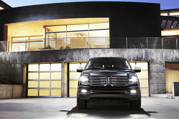 Front view of a black SUV with its headlights on in the evening at home