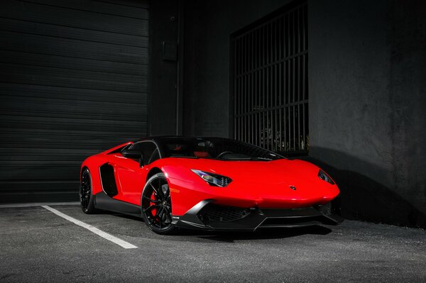 A red Lamborghini stands alone in a black garage