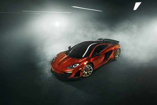 Pomarańczowy McLaren MP4-12C stoi w chmurze dymu