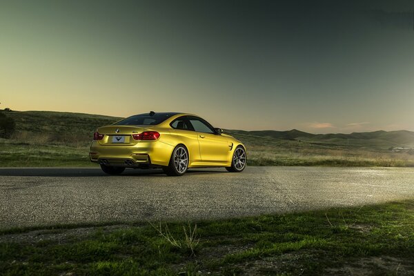 Un BMW M4 amarillo se encuentra en la carretera contra el fondo de las colinas