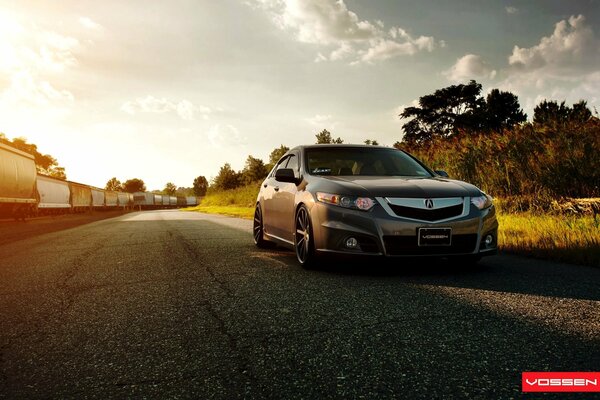 The acura tsx car is out of town. A freight train rides in the background