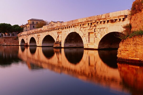 Reflection of an ancient bridge and a house in the water