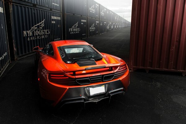 McLaren MP4-vx arancione passa tra i container marini