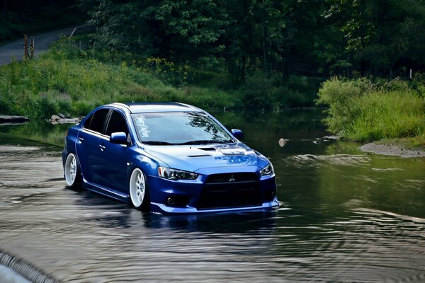 A blue Mitsubishi Lanzer car rides on water