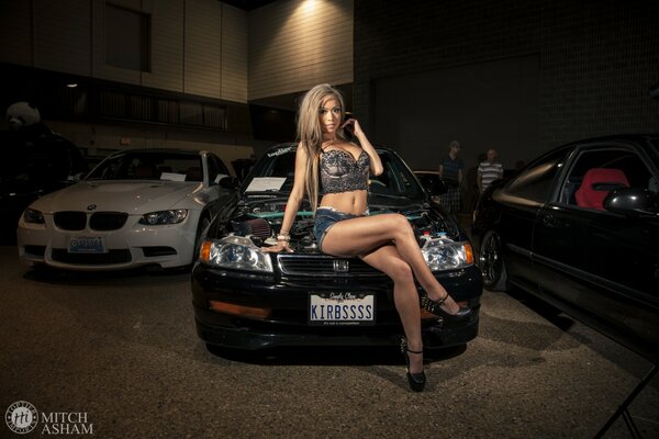 A girl is sitting on the hood of a racing car