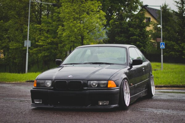 Tuning noir BMW E 36 sur fond d arbres verts