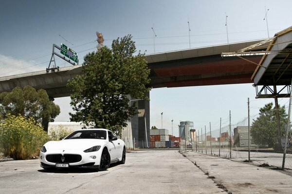 White maserati under the bridge next to the fence