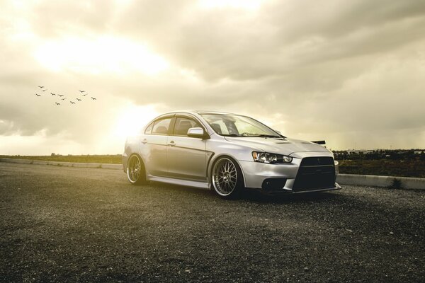 Silver Mitsubishi on the background of the sky with birds