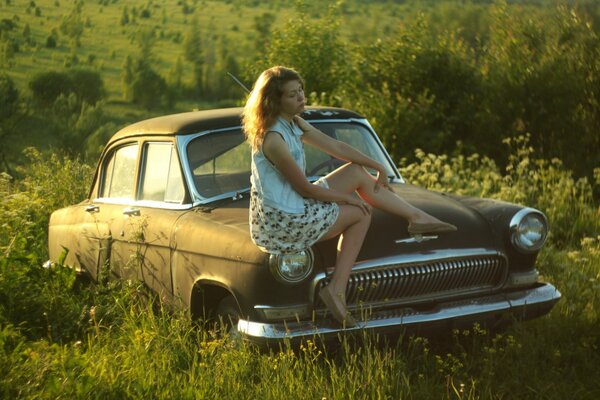 A girl in a good mood is sitting on a Volga car of the USSR times