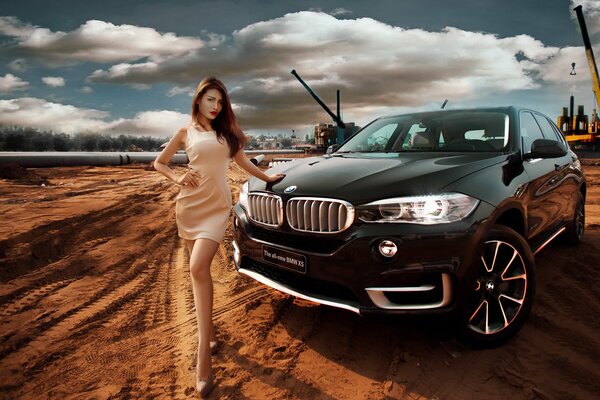 A girl next to a BMW on a construction site