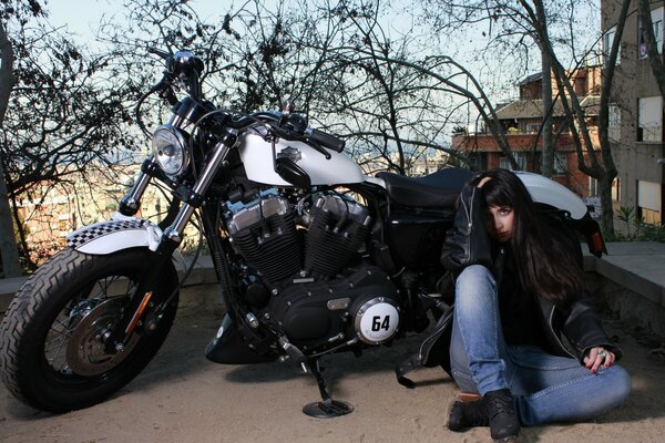 A girl is sitting on the street near a motorcycle