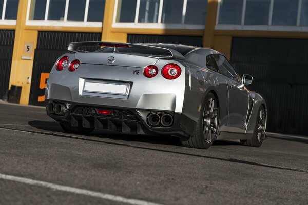 A gray Nissan rear view stands at an orange building