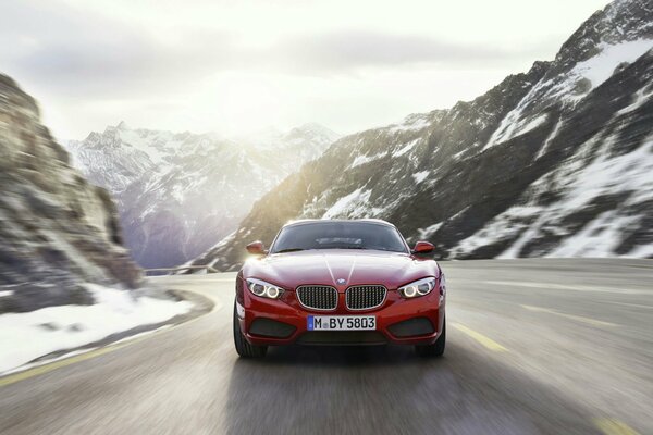 Sowohl die Berge im Schnee als auch die Sonnenstrahlen strahlen , und ein roter BMW fliegt auf der Strecke entlang