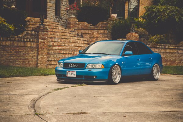 Blue Audi A4 in front of a brick fence