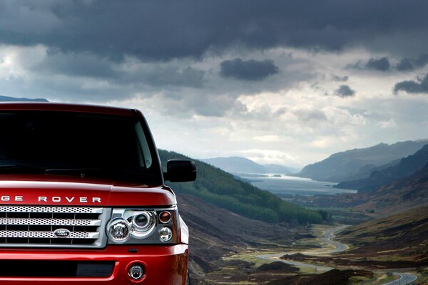 Auto rossa range rover sport sotto le nuvole nere del terreno di montagna