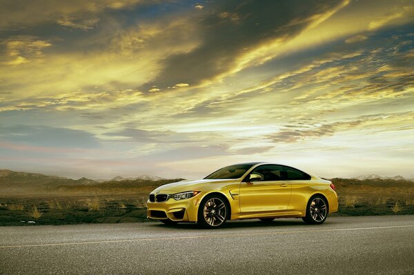 Золотистый автомобиль BMW M4 стоит на фоне красивого заката