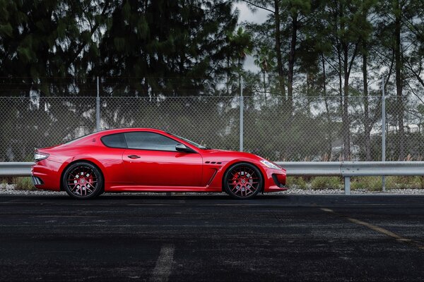 A red Maserati car stands on a fenced race track