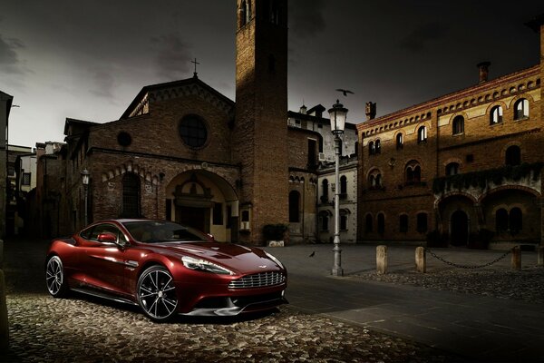 Voiture rouge aston martin m310 dans une cour semi-sombre