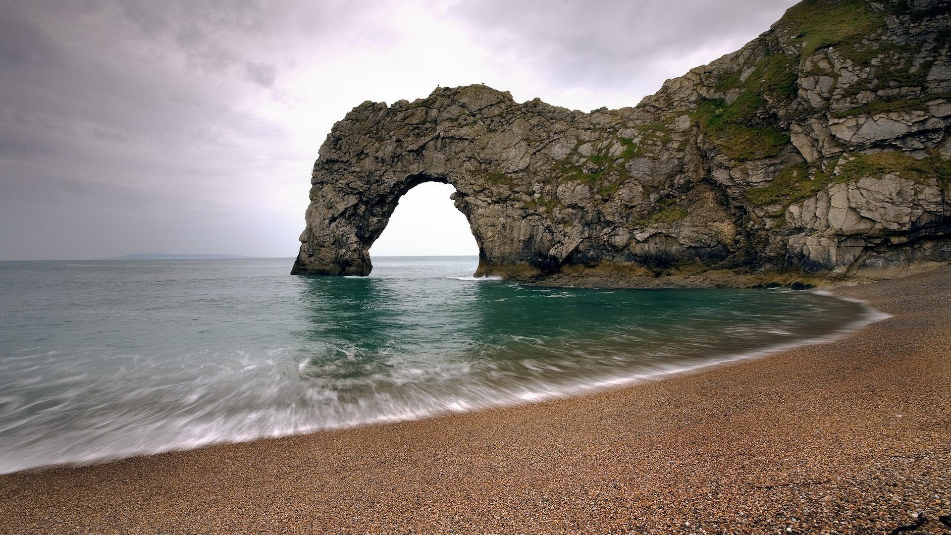 arch in the rock rocks sea beach water shore waves surf horizon nature cloudy arch rocks green water sand