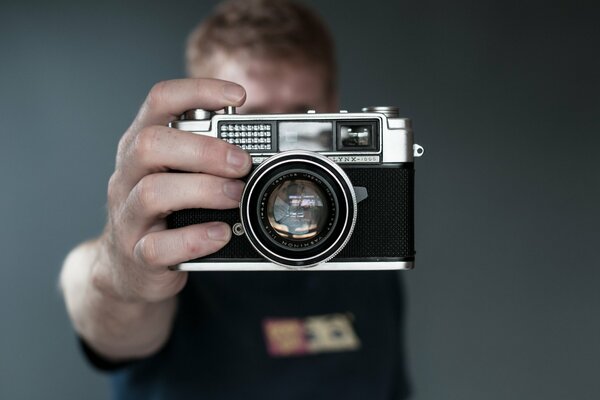 A man on a gray background holds a camera with his hand , his face is not visible