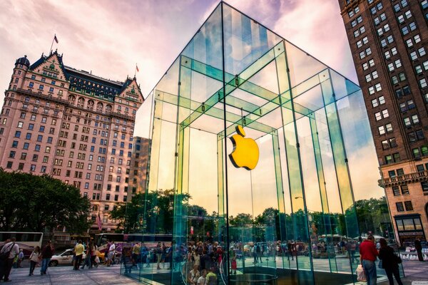 Die Straße, auf der Wolkenkratzer stehen, Menschen herumlaufen und in der Mitte ein Glasgebäude mit dem Apple-Logo