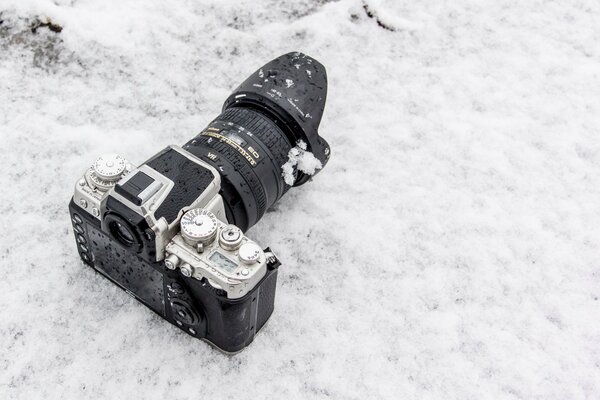 Eine Kamera mit einem großen Objektiv, die im Schnee liegt