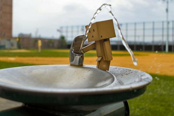 Ein Kastenmensch trinkt Wasser aus einem Brunnen