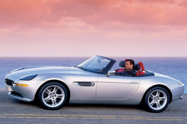 A man in a convertible on the seashore against the sunset