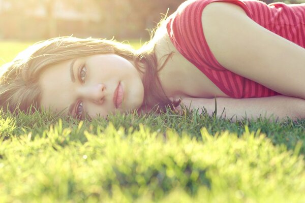 A girl poses lying on a sun - drenched green glade