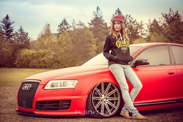 A girl is sitting on the hood of a red Audi