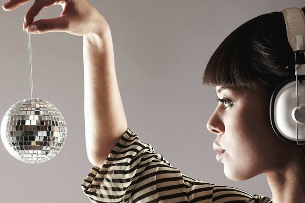 Brunette avec une frange dans les écouteurs tenant une petite boule disco