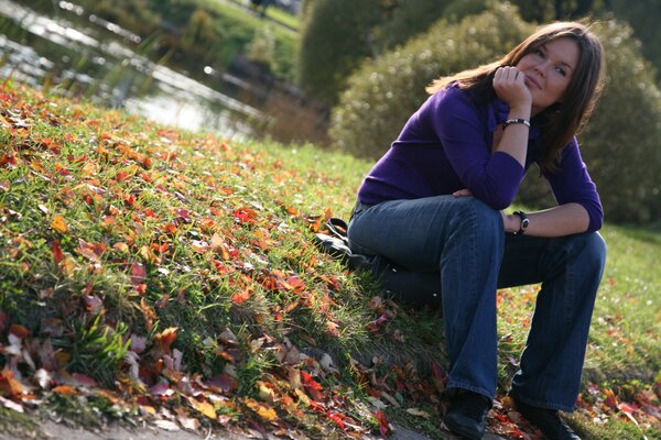 Chica sentada en la hierba con hojas de otoño