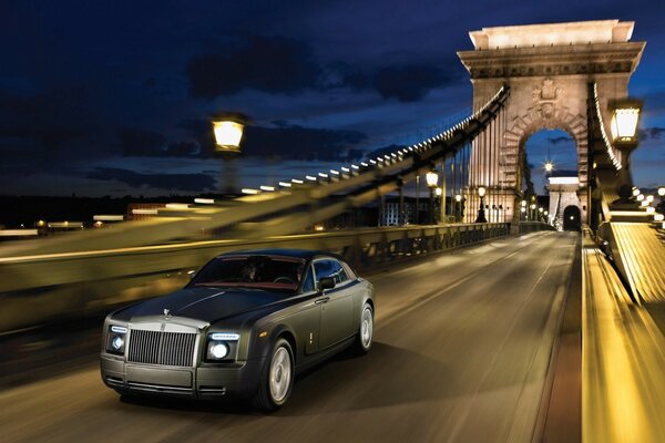 Grey matte Rolls Royce rushes across the bridge in the evening