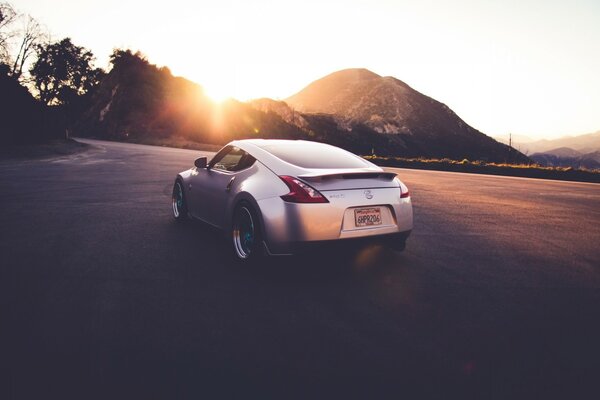 A silver car stands against the background of the setting sun