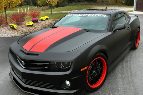 Chevrolet Camaro nero e rosso nel parcheggio vicino all aiuola