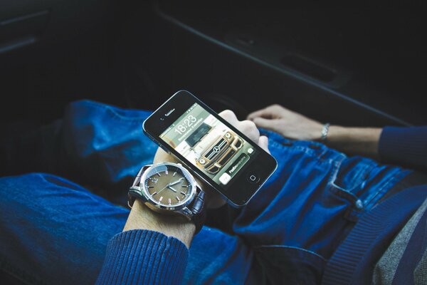 La mano con el reloj y el Teléfono descansa sobre sus pies en jeans