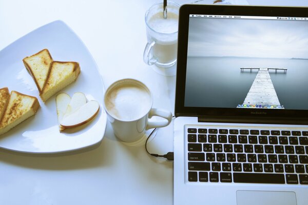 Travailler derrière un ordinateur portable pour une tasse de cappuccino et un dessert