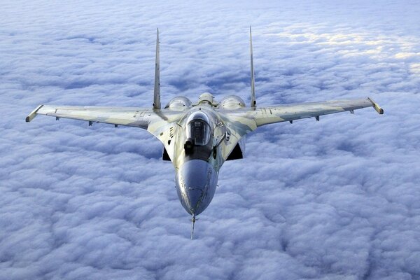 A grey fighter jet flies above the clouds