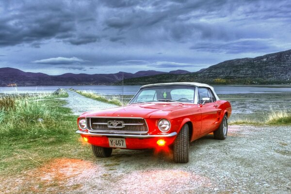 Mustang rosso vicino al lago con tempo nuvoloso