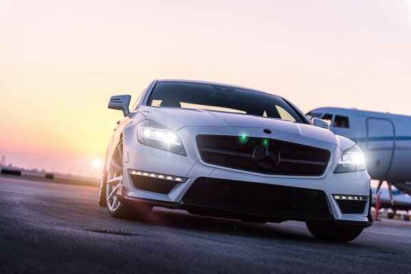 Mercedes di colore bianco in aeroporto sullo sfondo di un aereo