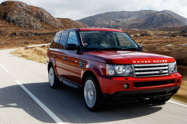 Auto rossa Renge Rover sulla strada sullo sfondo delle montagne