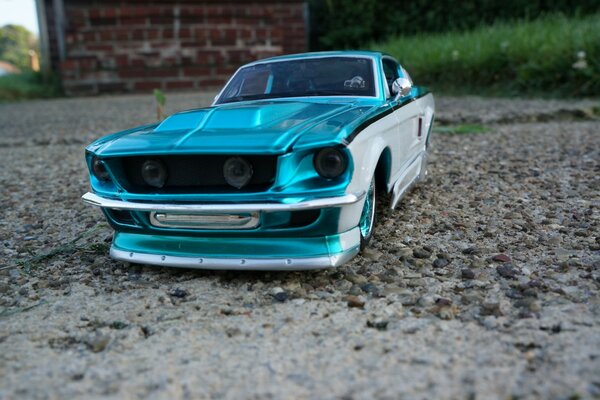 A model of a silver-blue Ford Mustang on an asphalt road