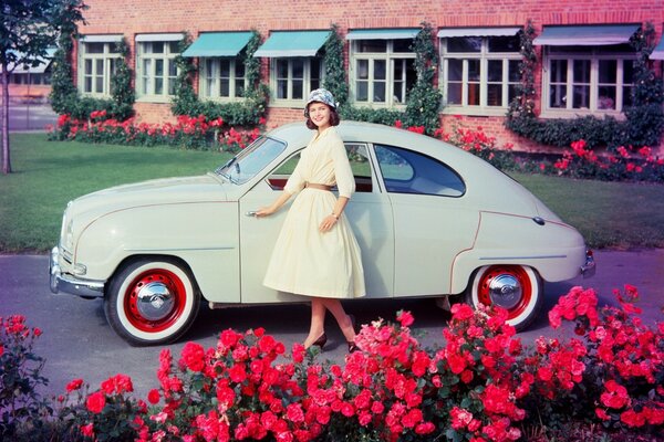 Hermosa chica y coche retro entre las flores