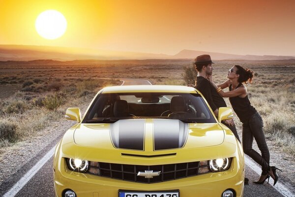 A road going beyond the horizon and a yellow chevrolet corvette with a girl and a guy