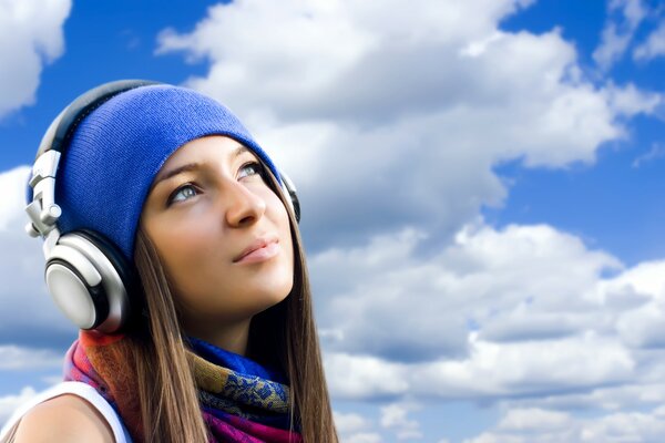 Beautiful girl with headphones on the sky background