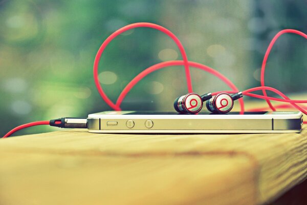 An iPhone with beats headphones lies on a wooden surface